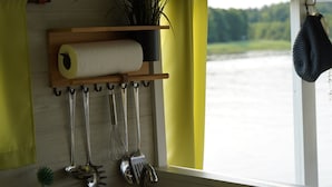 Een keuken met keukengerei dat aan haken hangt, een rol keukenpapier en een raam met uitzicht op het water.