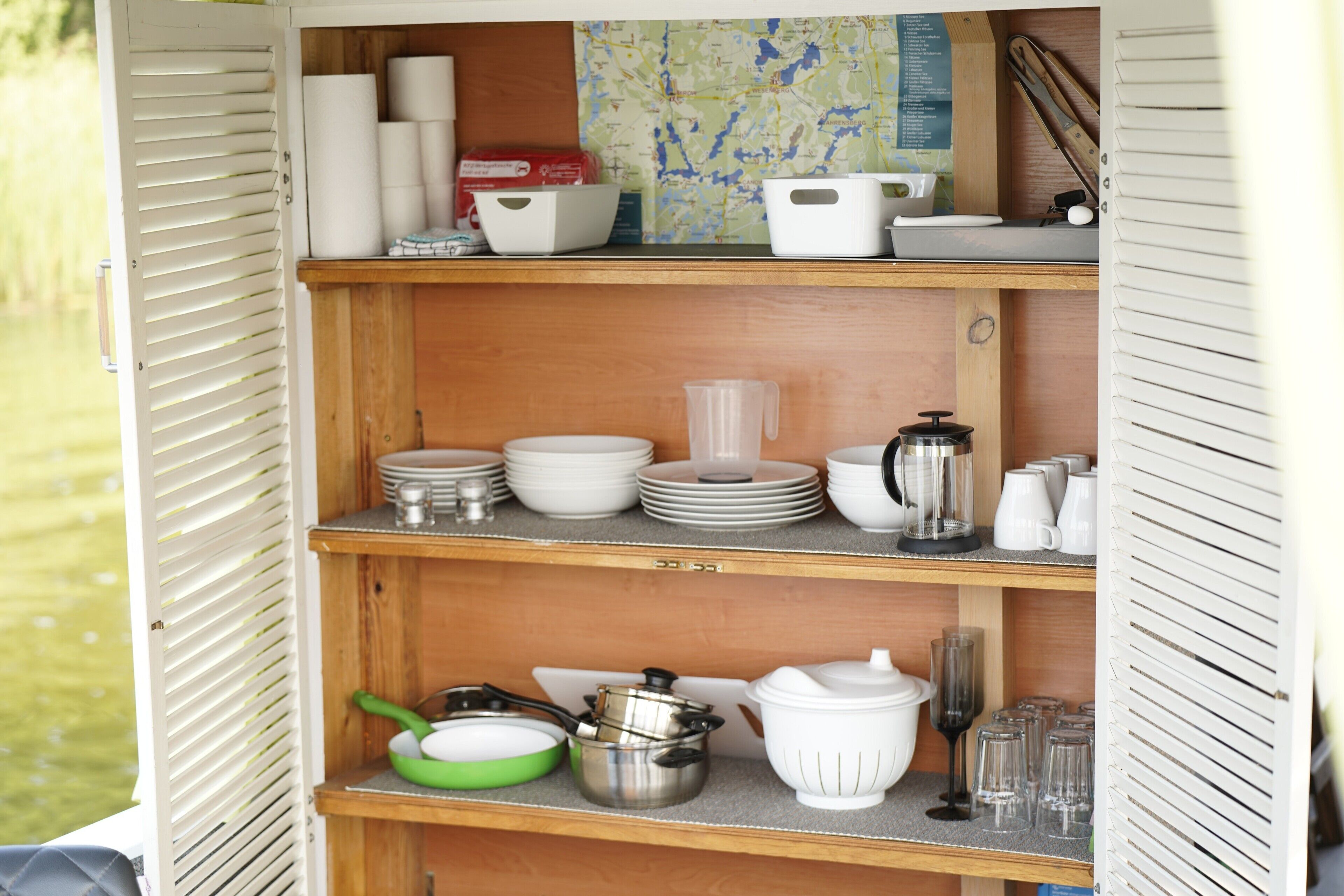 A kitchen with wooden shelves, white and green cookware, and a map on the wall.
