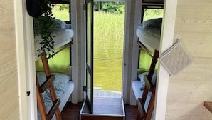 Een compact, modern interieur met stapelbedden, een klein zitgedeelte en uitzicht op een grasveld.