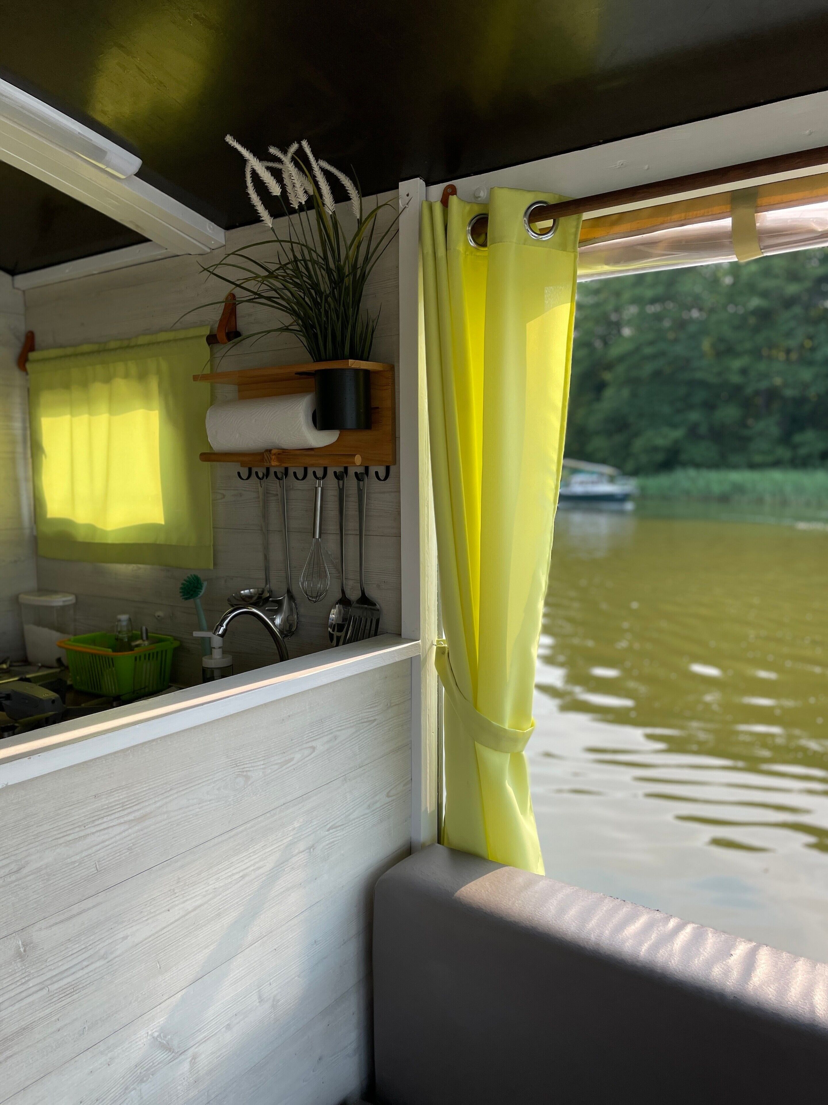 Eine Küche mit einer Holzausstattung, einer hängenden Pflanze und einem Fenster mit gelben Vorhängen.