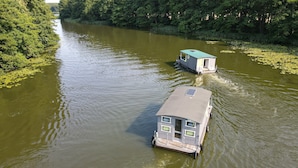 Een rijfloatwoning met een dek en ramen, drijvend op een rivier omringd door bomen.