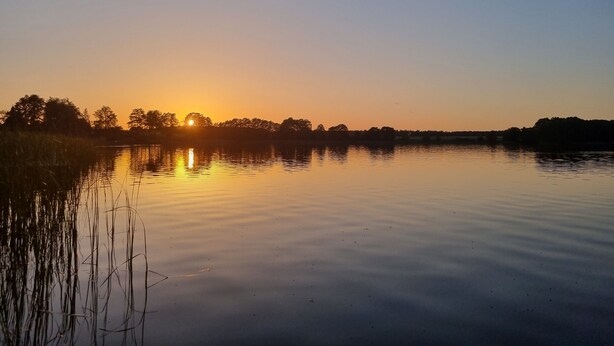 Un lac paisible au coucher du soleil, avec des arbres en arrière-plan.