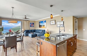 A modern kitchen with a central island, a dining area with a view, and a living room with a sofa and artwork.