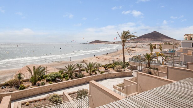 Eine Küstenlandschaft mit Strand, Palmen und Bergen im Hintergrund.