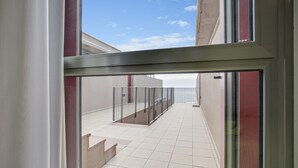 Blick durch eine Glastür auf einen Balkon mit Fliesenboden und Metallgeländer.