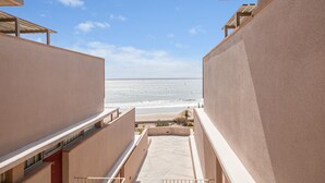 Blick vom Balkon eines Gebäudes auf einen Strand, mit blauem Himmel und ruhiger See.