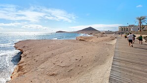 Une plage avec une promenade en bois, un rivage sablonneux et une montagne en arrière-plan.