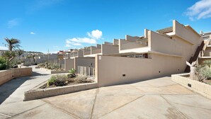 Un bâtiment moderne doté d’un toit plat, d’une cour avec un sol en pierre et de quelques plantes en pot.