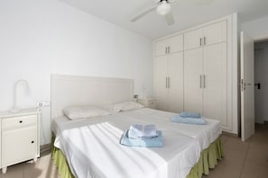A bedroom with two beds, a nightstand, a wardrobe, and a ceiling fan.