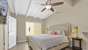Ein Schlafzimmer mit einem großen Bett, einem Deckenventilator, einem Fenster und einem Nachttisch.