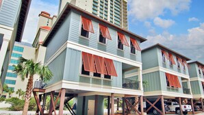A beachfront property with elevated structures, multiple windows with shutters, and a palm tree. - Hammock Dunes J (Orange Beach)