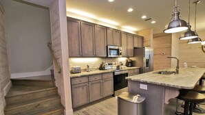 A modern kitchen with wooden cabinets, stainless steel appliances, a granite countertop, and a bar area. - Hammock Dunes J (Orange Beach)