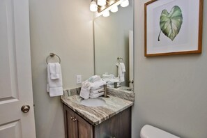 A bathroom with a marble sink, a mirror, and a framed plant. - Hammock Dunes J (Orange Beach)