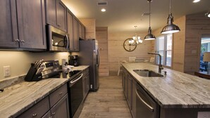 A modern kitchen with dark wood cabinets, stainless steel appliances, and a marble countertop. - Hammock Dunes J (Orange Beach)