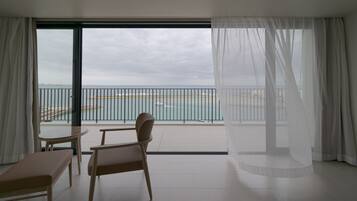 A balcony with a view of the sea and a boat, featuring a chair and a table.