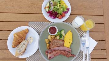 A breakfast setting with croissants, ham, potatoes, broccoli, and an omelette on a woven placemat.