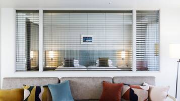 A modern living room with a sofa, multiple pillows, and large windows with blinds.