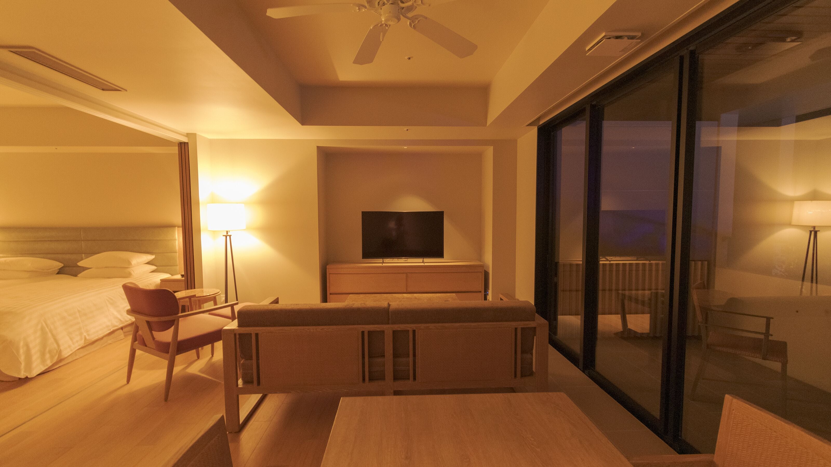 A hotel room with a bed, a TV, a sofa, a table, and a balcony with a view.