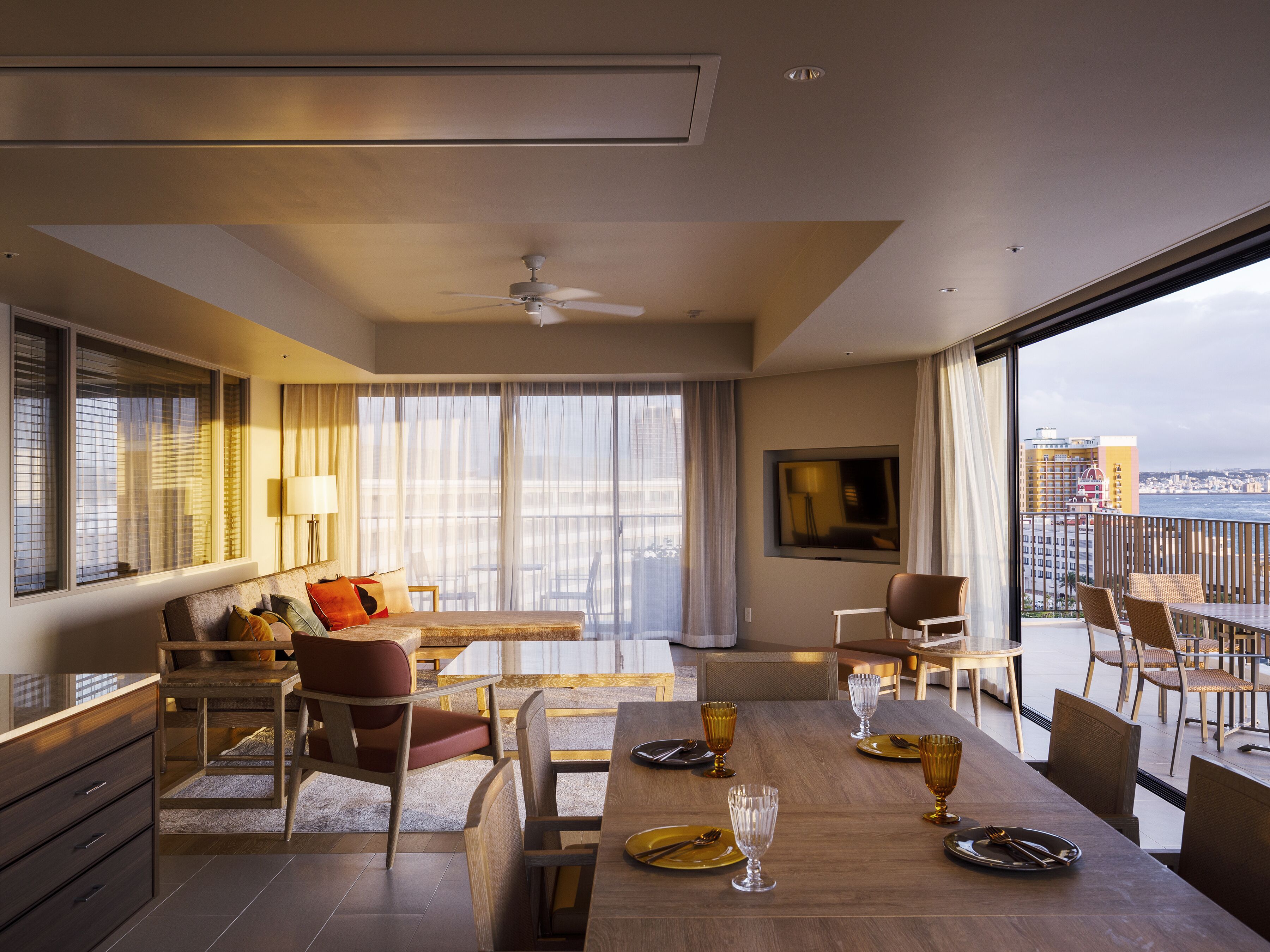A modern hotel room with a balcony, a dining area, and a large window offering a city view.