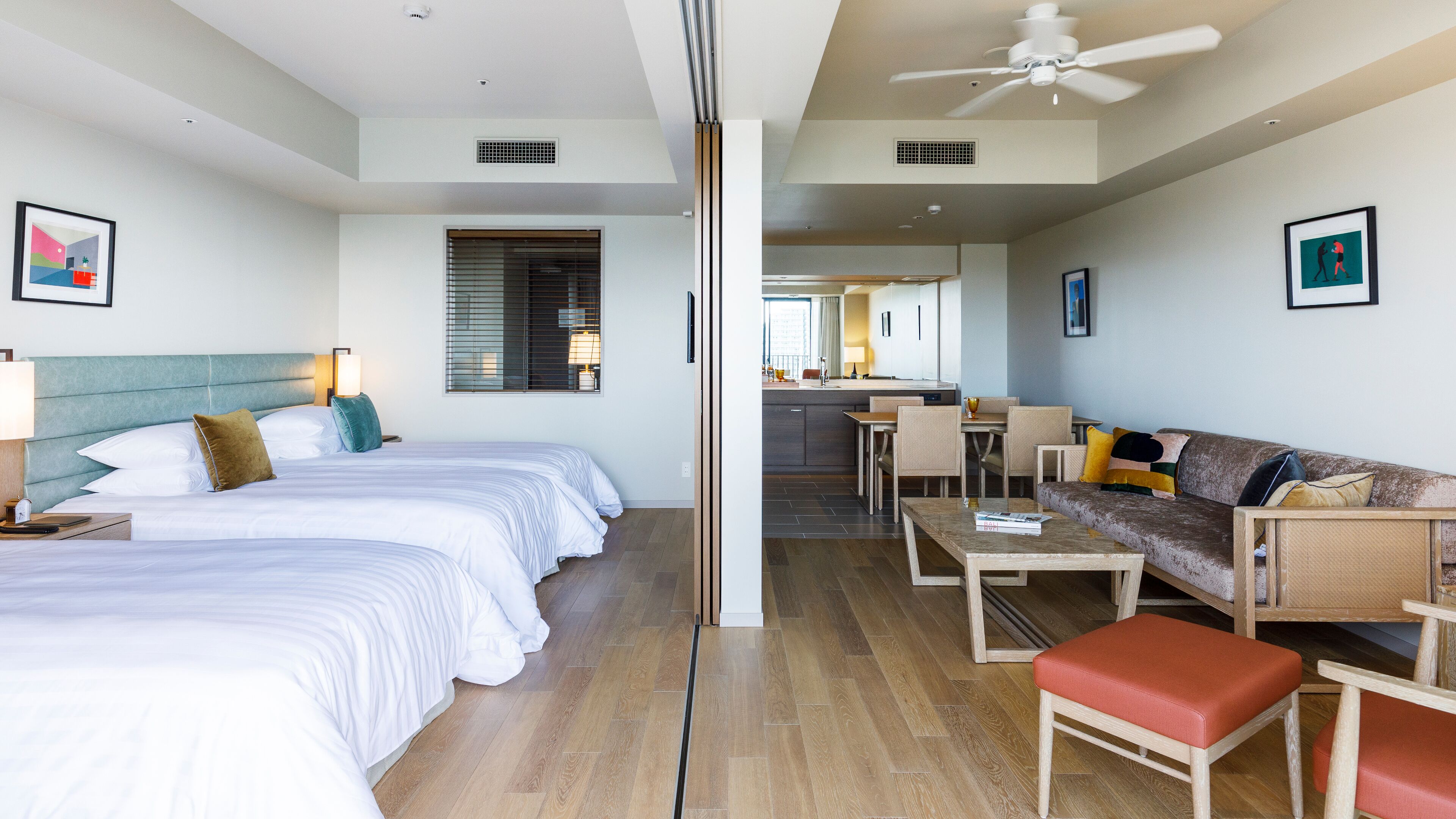A hotel room with a bed, a sofa, a dining table, and a kitchen area in the background.