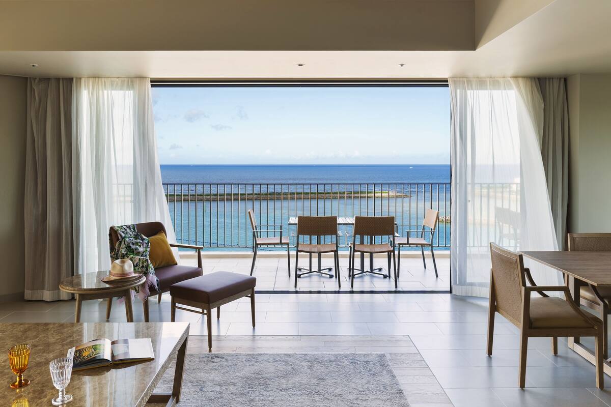 Uma varanda ampla com vista para o oceano, mobiliada com mesa, cadeiras e um sofá.