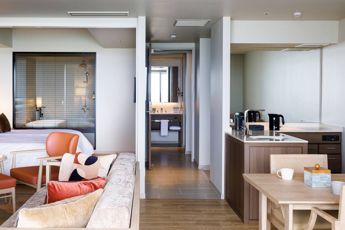 Quarto de hotel moderno com cama, sofá, mesa de jantar e cozinha.