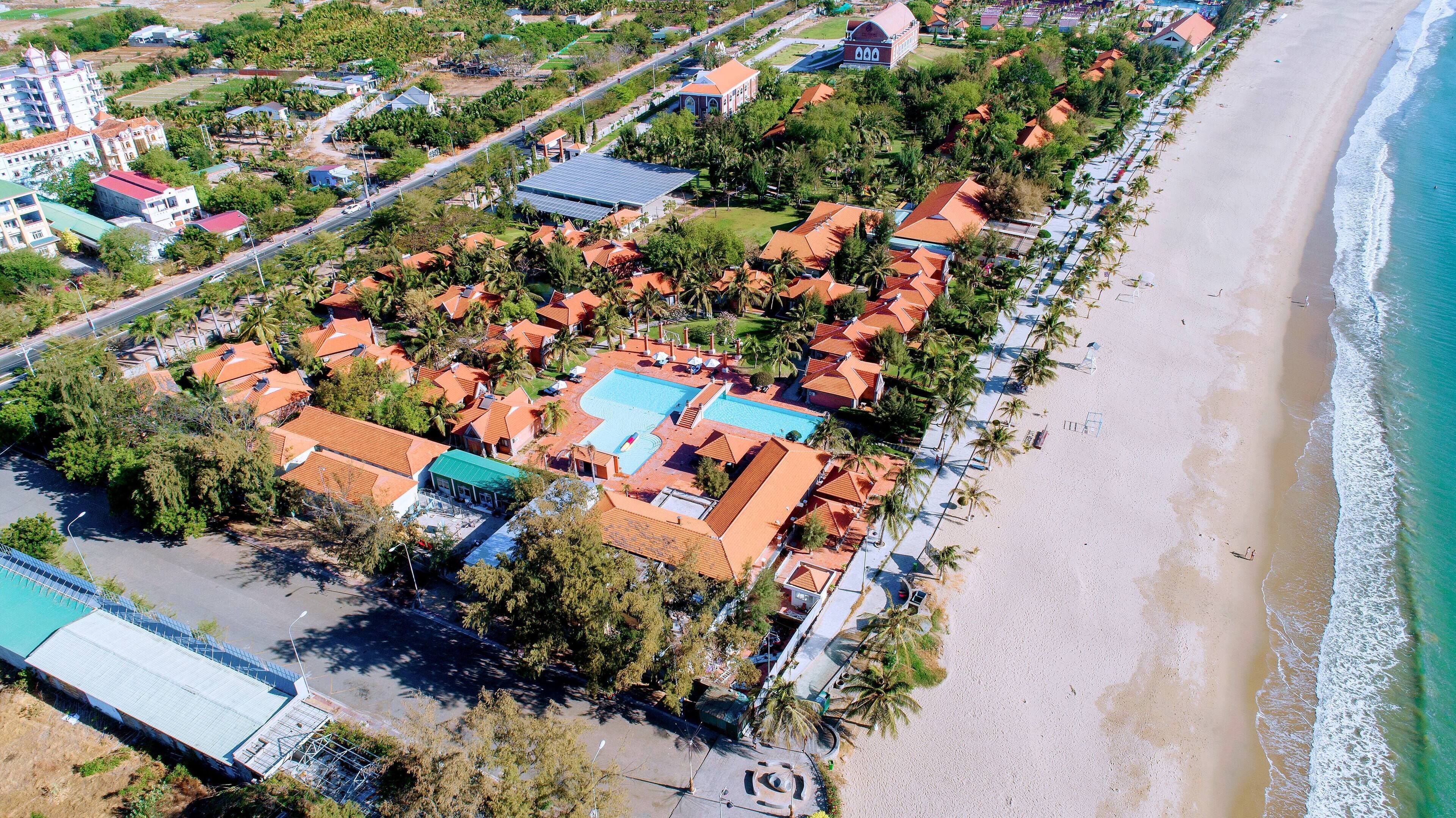 Vista aérea de una zona residencial costera con casas, una playa y un complejo de piscinas.