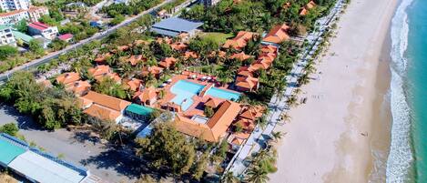 Vista aérea de una zona residencial costera con casas, una playa y un complejo de piscinas.