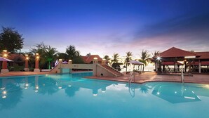 Una piscina con vista despejada al agua, un área de descanso techada y un edificio con tejado rojo.