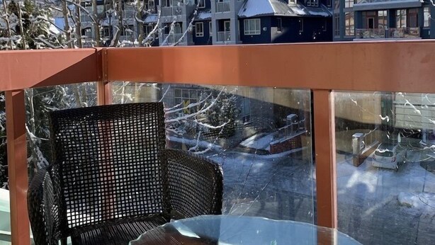 A balcony with a glass table and a wicker chair, overlooking a snowy mountain landscape and a row of houses. - Cozy, Bright Whistler Village Studio, Hot Tub, Sleeps 4 ( 2 adults 2 children)  (Whistler)