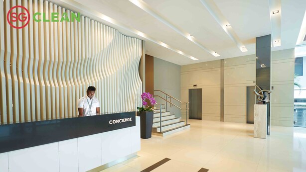 A hotel reception area with a modern design, a concierge desk, and a staircase leading to an elevator. - Wilby Central Serviced Apartments (Singapore)