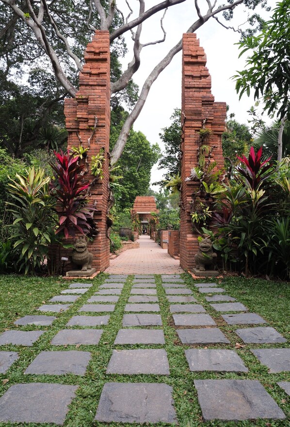 A pathway leading through a brick archway surrounded by lush greenery and a stone-tiled path.