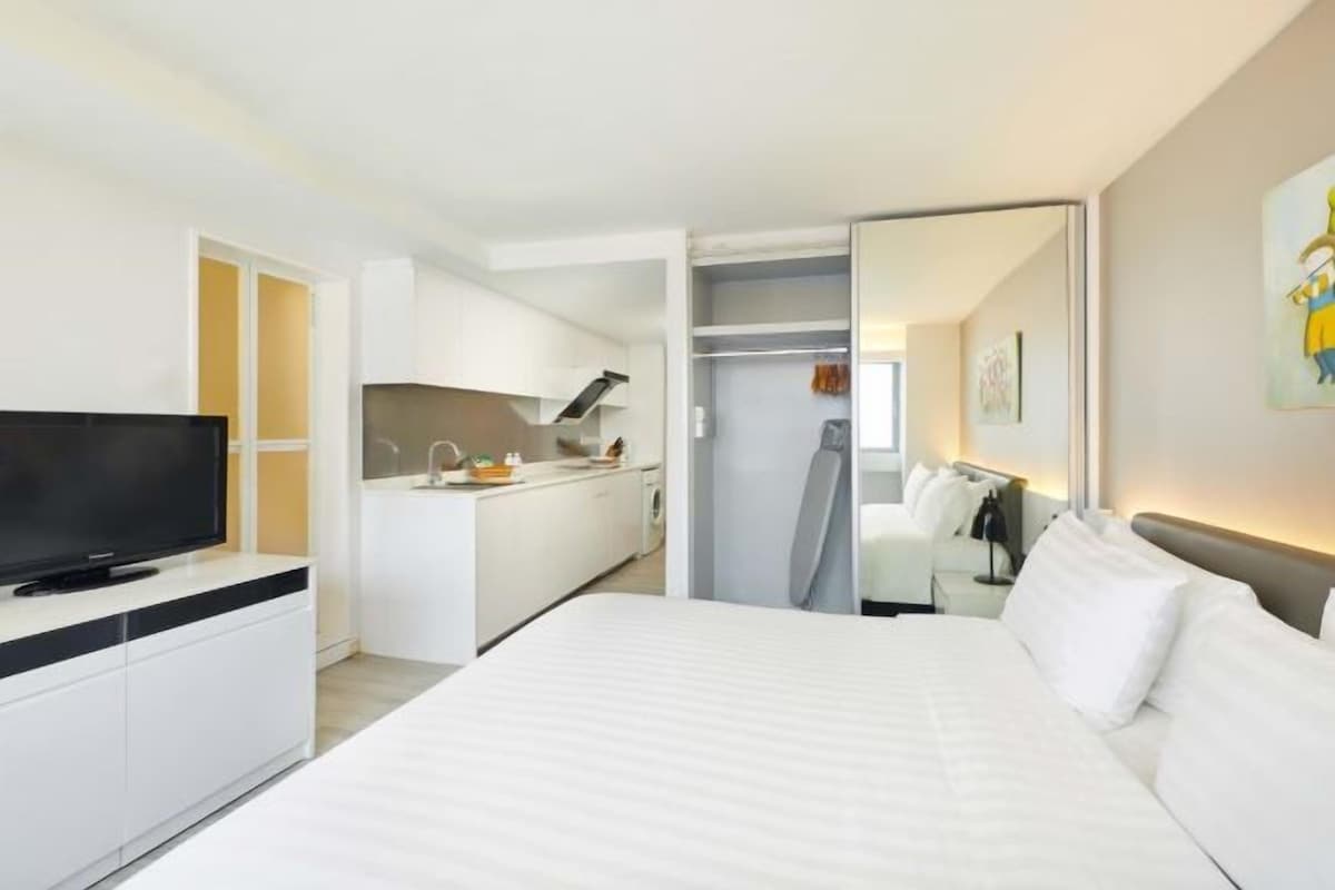A modern hotel room with a large bed, a TV, a kitchenette, and a bathroom.