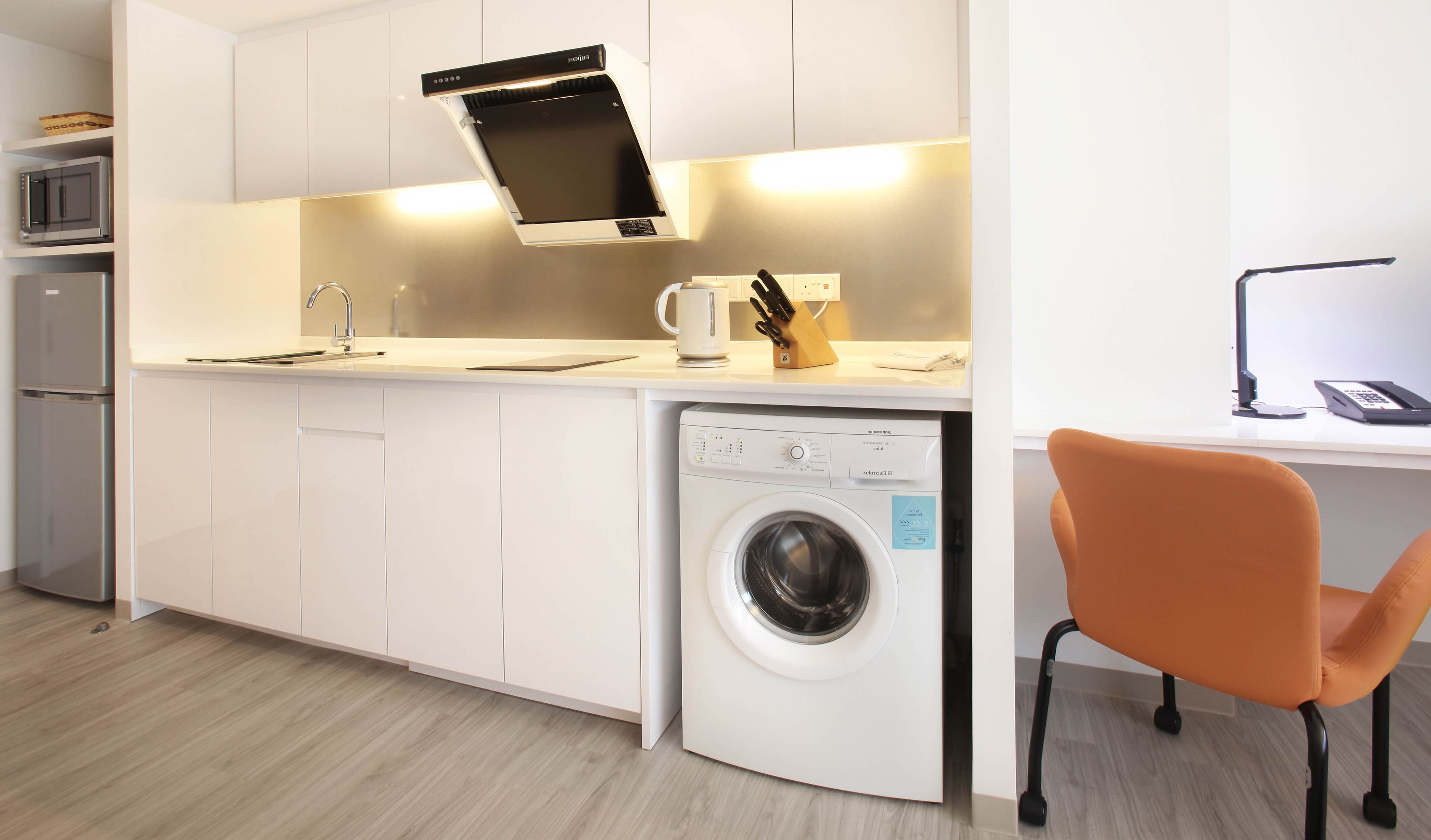 A compact kitchen with a built-in washing machine, a microwave, and a coffee maker.