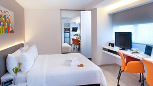 A hotel room with a bed, a desk with a computer, a TV, and a small kitchen area in the background. - Wilby Central Serviced Apartments (Singapore)