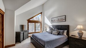Un dormitorio con una cama grande, un aparador, un televisor y una ventana con vistas a árboles.