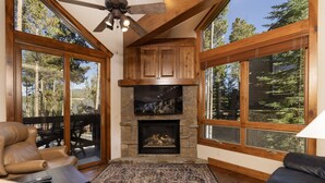 Una sala de estar acogedora con chimenea de piedra, sofás de cuero y grandes ventanales con vistas al bosque.