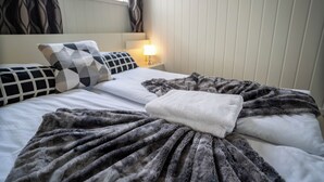 A neatly made bed with a gray blanket and a white towel, a patterned pillow, and a bedside lamp.