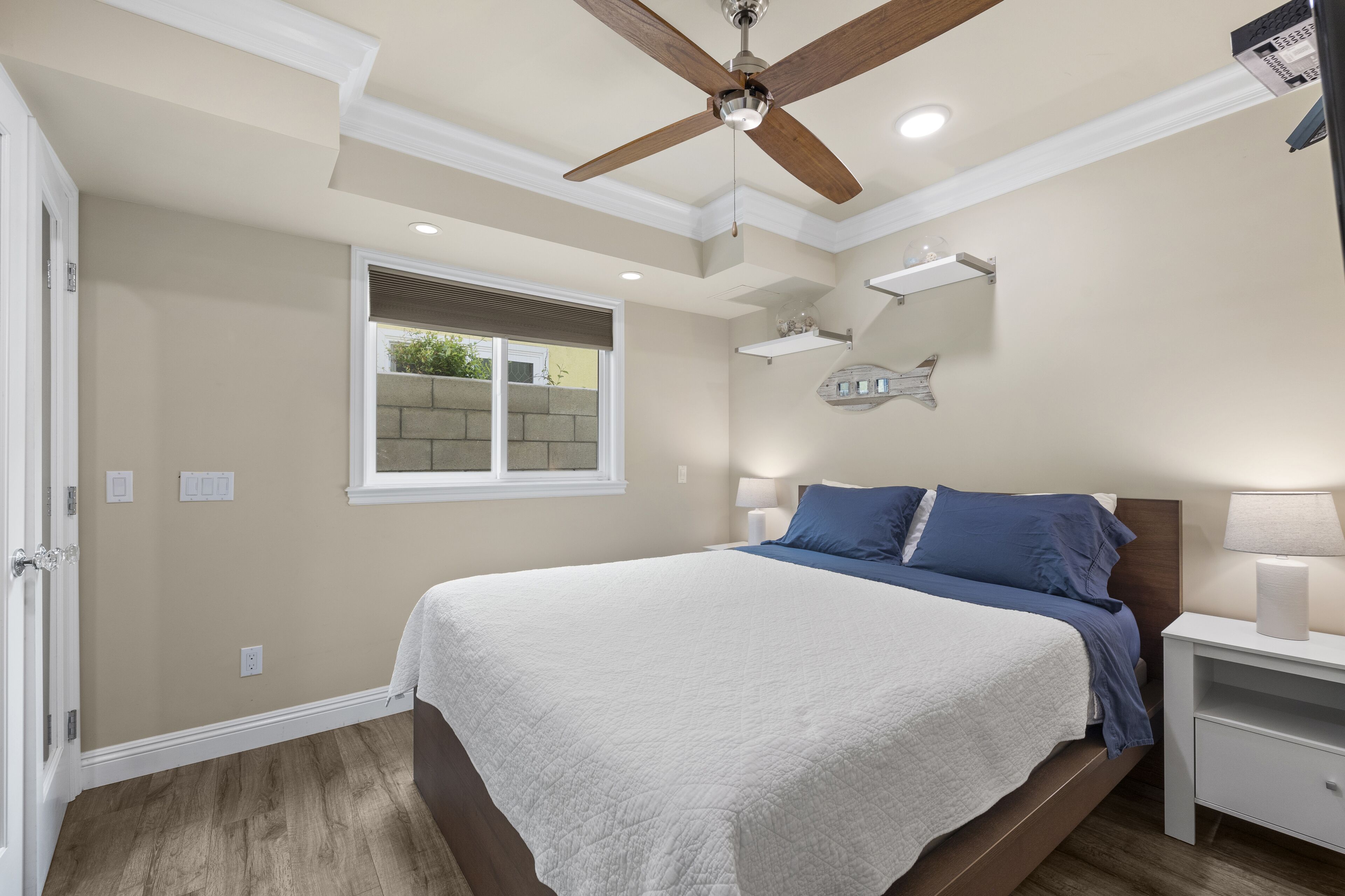 Une chambre à coucher avec un lit, des tables de chevet, un ventilateur de plafond et une fenêtre.