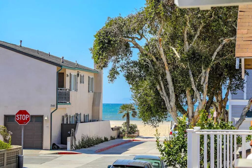 A coastal residential area with a stop sign, a white building with a garage, and a view of the beach.
