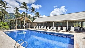 Une piscine avec des chaises longues, un espace salon couvert et des palmiers en arrière-plan.
