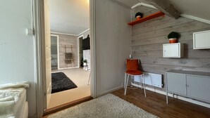 En modern inredning med ett trägolv, en vit dörr, en liten orange stol, ett vitt skåp och en hylla med växter.