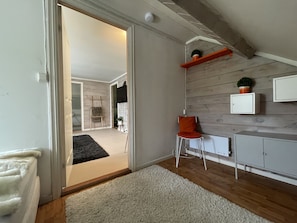 A modern interior with a wooden floor, a white door, a small orange chair, a white cabinet, and a shelf with plants.