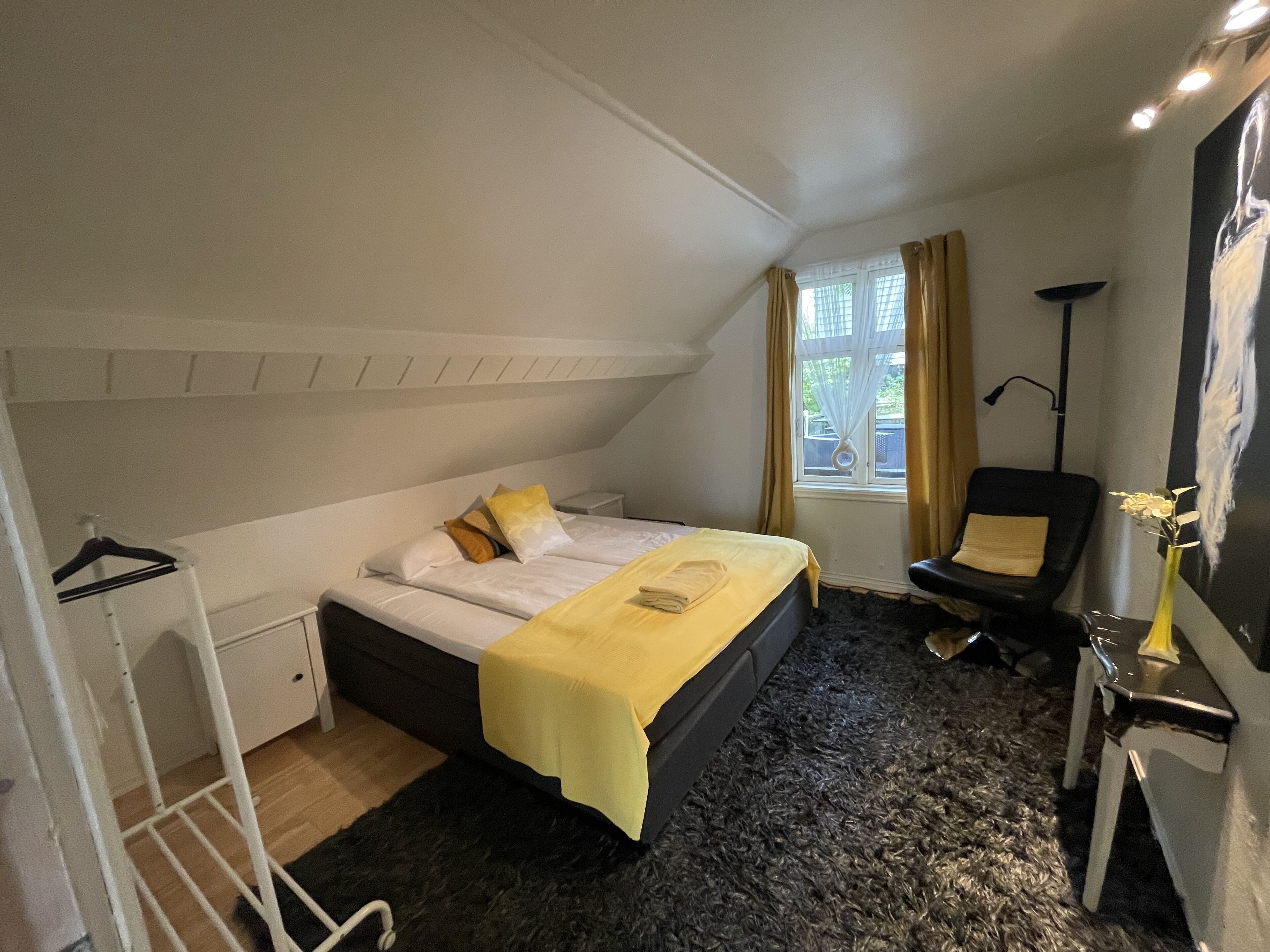 Et soveværelse med seng, stol, skrivebord, lampe og et vindue med gardiner.