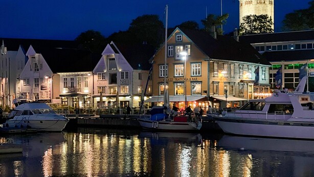 Ett område vid vattnet med byggnader, inklusive en restaurang och en bar, och flera båtar förtöjda.