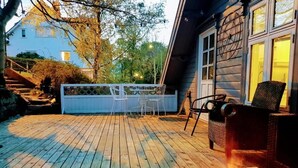 En träaltan med utemöbler, en grill och ett hus i bakgrunden.