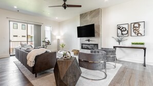 A modern living room with a sofa, coffee table, and ottoman, a flat-screen TV mounted on the wall, and a fireplace. - Brand new Bishop Arts Condo-Right in the middle of it all! Three bathrooms! (Dallas)