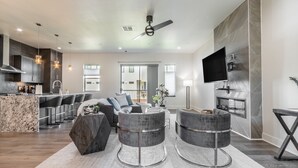 A modern living room with a large L-shaped sofa, two round grey ottomans, a marble accent wall, a flat-screen TV mounted on the wall, and a ceiling fan. - Brand new Bishop Arts Condo-Right in the middle of it all! Three bathrooms! (Dallas)