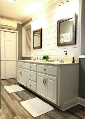 Un baño con muebles blancos, un espejo grande y suelo de madera.