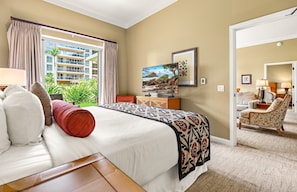 A hotel room with a bed, a television, a window with curtains, a door, and a view of a building outside. - Maui Resort Rentals: Honua Kai - 4 Total Bedrooms, Ground Floor Interior Courtyard, Steps to Pools, Beach, BBQs! (Lahaina)